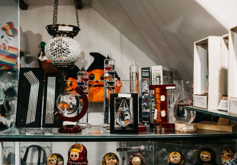 A shop shelf of galileo thermometers, a mosaic lantern and painted nesting dolls.