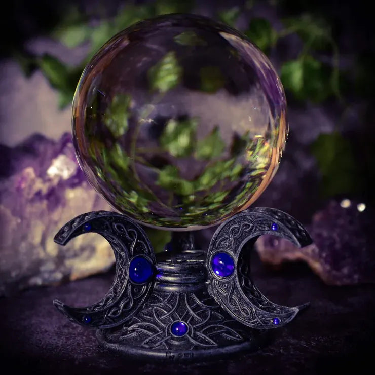 A crystal ball resting on a carved triple moon stand.